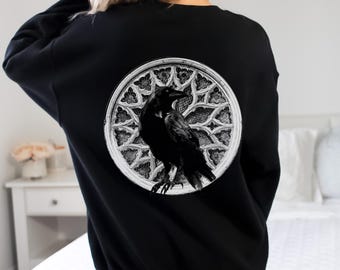 May include: Black sweatshirt with a graphic of a black raven in a white gothic window design.