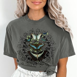 May include: A gray t-shirt with a graphic of a mandala design featuring butterflies in shades of blue, green, and black.