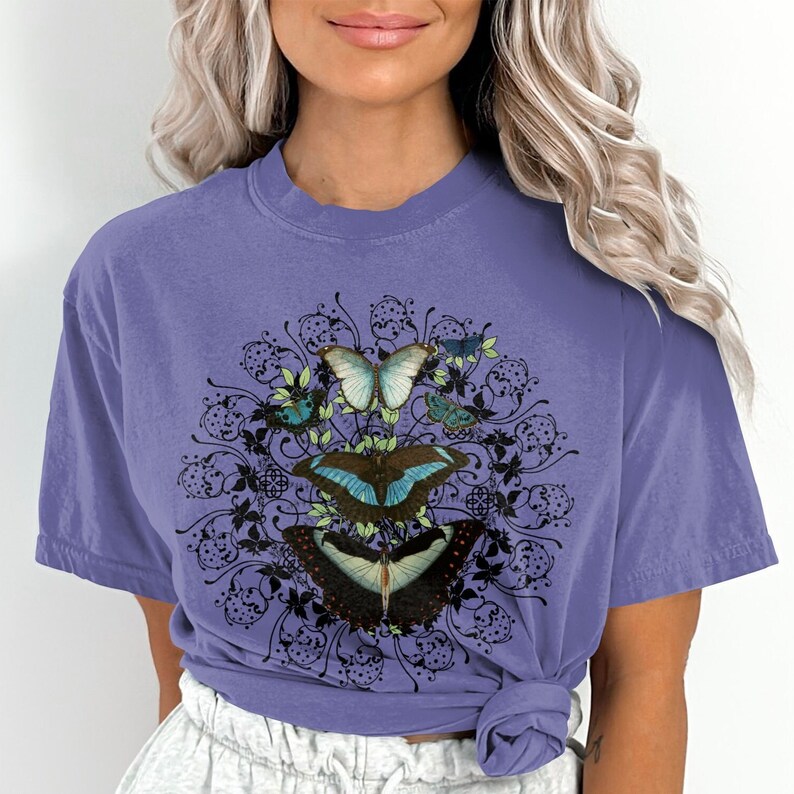 May include: A purple t-shirt with a graphic of a mandala design featuring butterflies in shades of blue, green, and black.