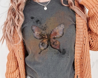 May include: A gray t-shirt with a watercolor butterfly design in shades of brown, orange, and black. The butterfly is centered on the shirt and has a distressed, vintage look.