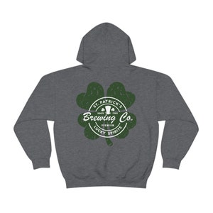 May include: A dark gray hoodie featuring a green shamrock design with the text "St. Patrick's Brewing Co. Premium Lucky Spirits" in white. The hoodie has a hood and long sleeves.