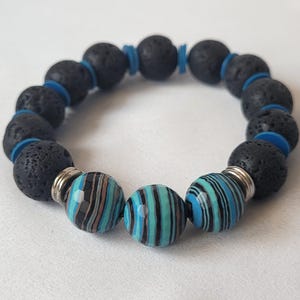 May include: A beaded bracelet featuring black lava rock beads, blue spacers, and three striped beads in shades of blue, black, and brown. The bracelet has a silver-colored metal accent on each of the striped beads.