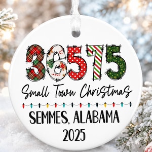 May include: A white ceramic Christmas ornament with the text "36575 Small Town Christmas SEMMES, ALABAMA 2025". The numbers are in festive patterns of plaid, polka dots, and green glitter. A string is attached for hanging.