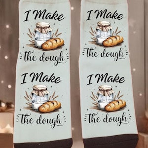 Puede incluir: Par de calcetines blancos con talón y puntera negros, con un gráfico de un tarro, pan y trigo. El texto "I Make the dough" está impreso en los calcetines, con la frase repetida dos veces.