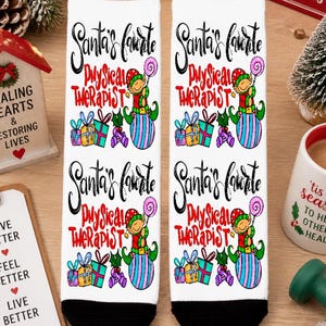 Può includere: Calzini bianchi con la scritta "Santa's Favorite Physical Therapist" e un disegno di elfo. I calzini hanno tallone e punta neri. L'immagine include decorazioni natalizie e una tazza.