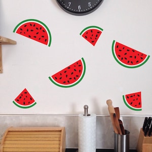 May include: A white wall with six red watermelon slice decals. The watermelon slices are various sizes and are arranged in a random pattern.