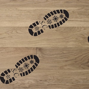 May include: Black boot print design with snowflakes and the letters "S.C." on a light brown wooden surface. The boot prints are arranged diagonally across the wooden planks, creating a pattern.