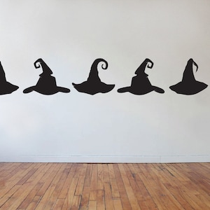 May include: A row of eight black witch hat silhouettes on a white wall. The hats are all the same shape, but they are arranged in a staggered pattern.