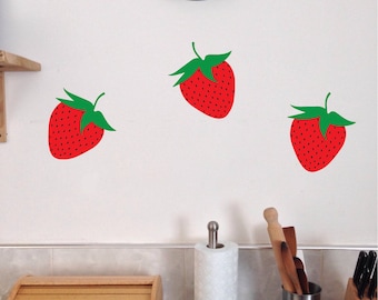 May include: Three red strawberry wall decals with green leaves on a white wall.