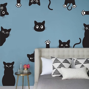 May include: A blue wall with black cat silhouettes, including a cat peeking from behind a headboard of a bed with gray bedding and pillows. The pillows have a geometric pattern.