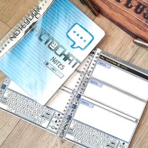May include: Spiral-bound notebooks with a blue and white cover featuring the text "PICTOCHAT NOTES" and a speech bubble graphic. The open notebook pages have a keyboard design and space for notes. The notebooks are on a wooden surface.