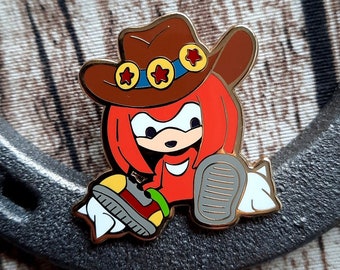 May include: A gold-colored enamel pin featuring a cartoon character wearing a brown cowboy hat with gold stars. The character is red with white eyes and a white mouth. The character is sitting with one leg bent and the other leg extended. The character is holding a white object in its hand.