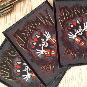 May include: Three black patches with a cartoon character in red and black, white gloves, and red shoes. The patches have the text "NIGHT HERO" and are next to two toy revolvers.