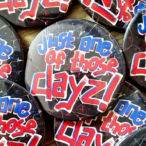 May include: A collection of round buttons with the phrase "Just One of Those Dayz!" in red and blue graffiti-style lettering. The buttons have a black background with a cracked texture.