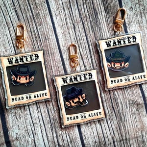 May include: Three gold keychains with cartoon characters on them. Each keychain has a brown and white wanted poster with the text "WANTED DEAD OR ALIVE".