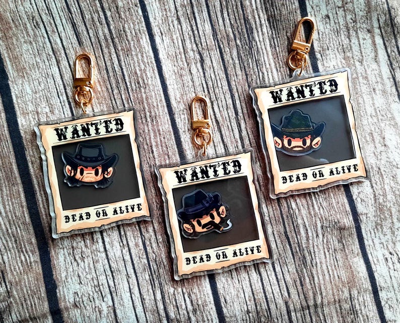 May include: Three gold keychains with cartoon characters on them. Each keychain has a brown and white wanted poster with the text "WANTED DEAD OR ALIVE".
