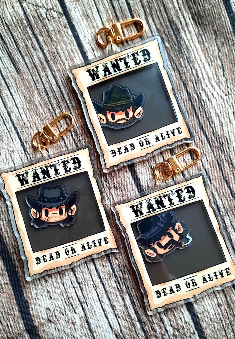 May include: Three clear acrylic keychains with gold metal clasps. Each keychain features a cartoon character with a cowboy hat and mustache. The background of each keychain is a vintage-style "WANTED" poster with the text "DEAD OR ALIVE".
