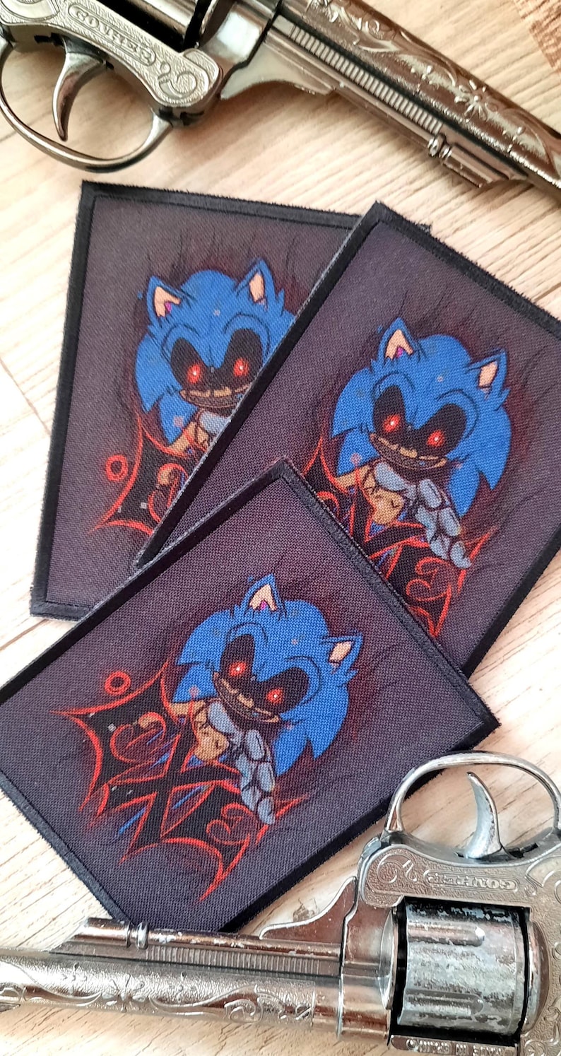 May include: Three rectangular patches featuring a blue cartoon character with red eyes and a sinister expression. The patches are on a dark background with red accents. Two silver toy revolvers are in the background.