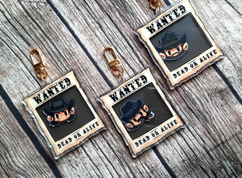 May include: Three gold keychains with a cartoon character wearing a cowboy hat and a wanted poster design. The poster says "WANTED" and "DEAD OR ALIVE".
