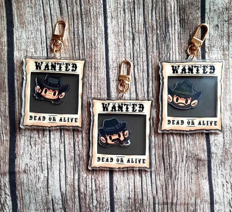May include: Three keychains with a wanted poster design. Each keychain features a cartoon character with a cowboy hat and the text "WANTED DEAD OR ALIVE".