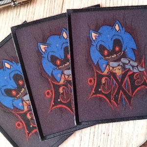 May include: Three square patches featuring a blue cartoon character with red eyes and the word "EXE" in red. The patches are on a wooden surface, with two toy revolvers in the background.