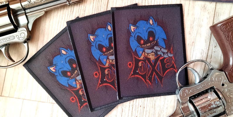 May include: Three square patches featuring a blue cartoon character with red eyes and the word "EXE" in red. The patches are on a wooden surface, with two toy revolvers in the background.