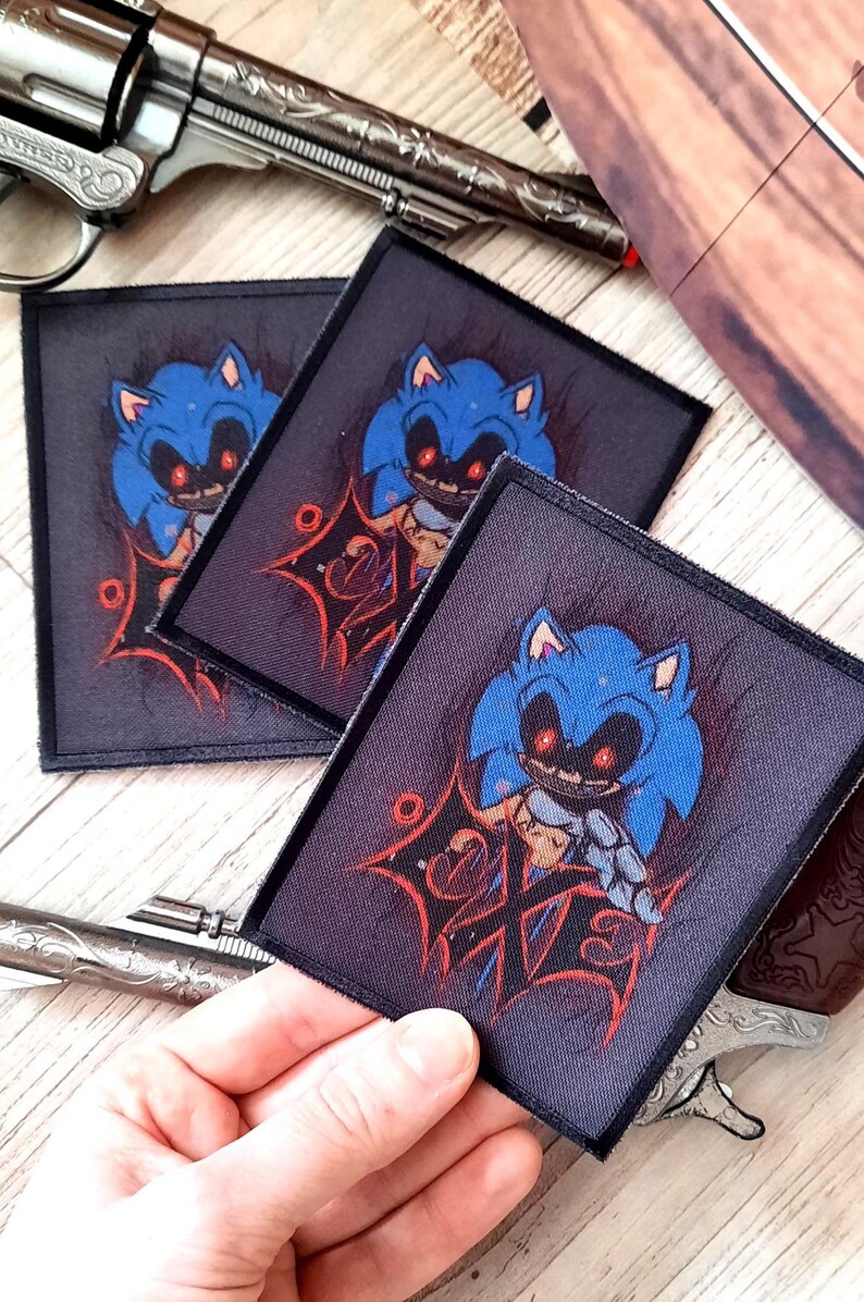 May include: Square patches featuring a blue cartoon character with red eyes and a sinister grin. The patches have a dark background with red accents and are surrounded by a black border. The patches are displayed near a silver revolver.