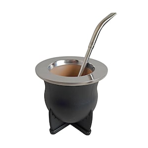 May include: A matte black mate gourd with a smooth, rounded body and a wide, polished silver-colored metal rim. The vessel rests on a sturdy, integrated black cross-shaped base and includes a long, slender, polished silver-colored metal bombilla straw.