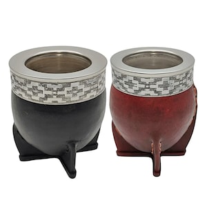 May include: Two mate gourds, one black and one dark red, each featuring a silver-colored metal rim with a geometric pattern. Both gourds are supported by three-legged stands matching their respective colors and have smooth, rounded bodies.