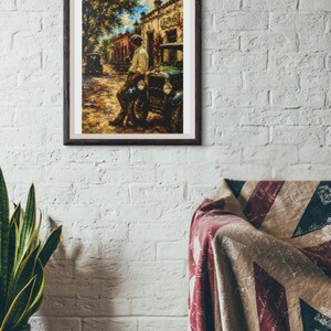 May include: A framed wall art print depicting a street scene with a person leaning against a vintage car. The artwork features a warm color palette with yellow, brown, and blue tones, showcasing a building in the background and a tree on the left.