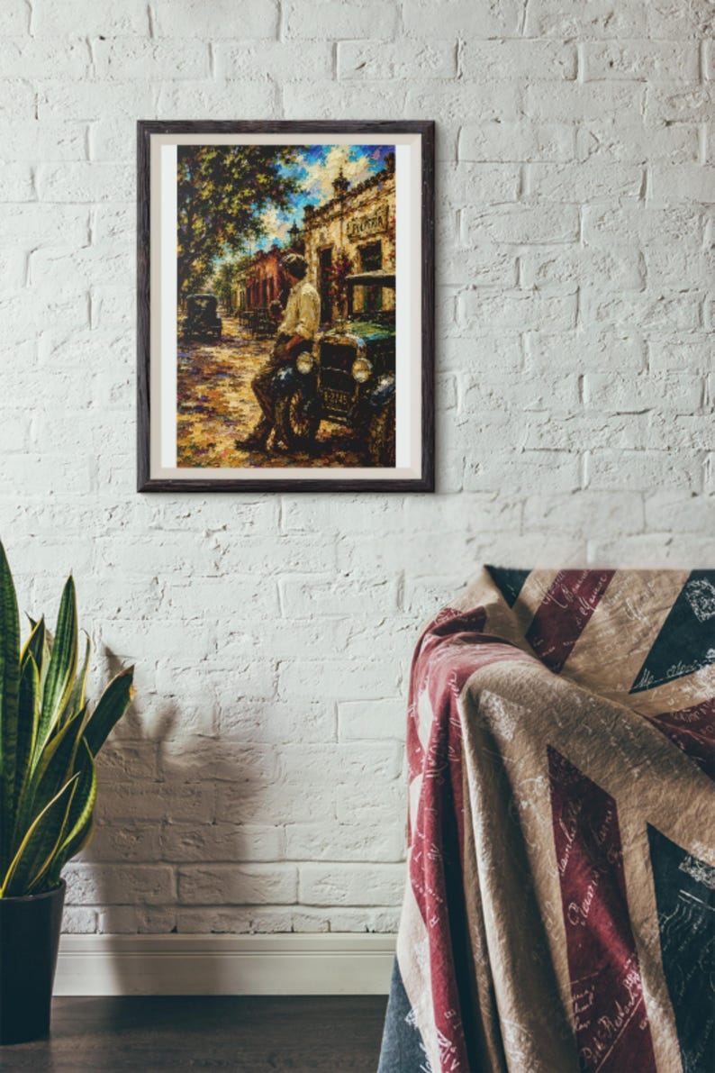 May include: A framed wall art print depicting a street scene with a person leaning against a vintage car. The artwork features a warm color palette with yellow, brown, and blue tones, showcasing a building in the background and a tree on the left.