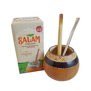 Può includere: Una confezione da 250g di Yerba Mate Salam con un grafico di un campo verde e testo rosso, accanto a una zucca rotonda marrone con motivo geometrico e due cannucce, una beige chiaro e una color argento, inserite nell'apertura.