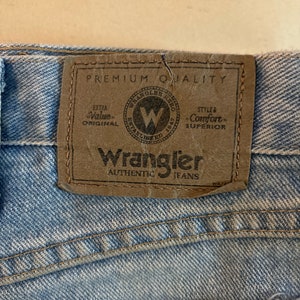 May include: A close-up of a brown leather patch sewn onto a pair of blue denim jeans. The patch has the text "Wrangler Authentic Jeans" and a logo with the text "Wrangler" and "Established 1947". The patch also has the text "Premium Quality", "Extra Value Original", and "Style & Comfort Superior".