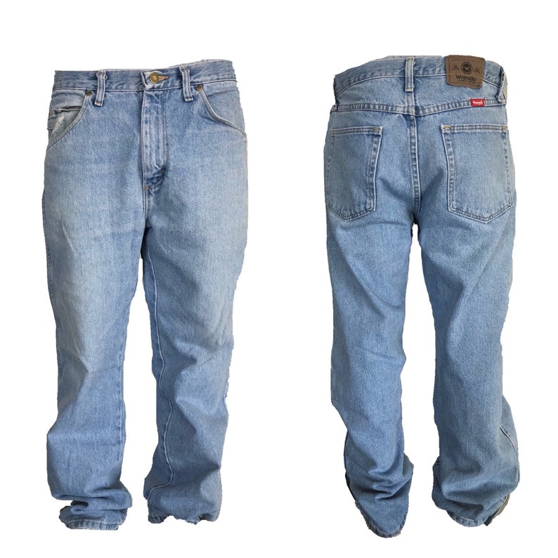 Puede incluir: Vaqueros de mezclilla azul claro, vista frontal y trasera, con un dise&ntilde;o cl&aacute;sico de cinco bolsillos. Los vaqueros tienen cierre de bot&oacute;n y cremallera, trabillas para el cintur&oacute;n y un parche de cuero marr&oacute;n con el logo de Wrangler en la parte trasera.