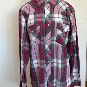 May include: A long-sleeved plaid shirt with a red, white, green, and blue plaid pattern. The shirt has a button-down collar and two chest pockets.