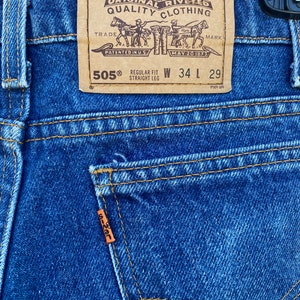May include: A close-up of a blue denim Levi's 505® jeans label with the text "ORIGINAL RIVETED QUALITY CLOTHING" and "REGULAR FIT STRAIGHT LEG" with the size tag "W 34 L 29".