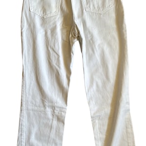 May include: A pair of white denim jeans with a straight leg fit. The jeans have a classic five-pocket design and a button fly.