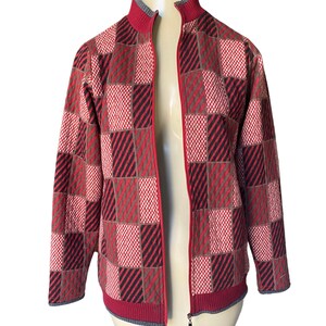 May include: A red, brown, and black checkered zip-up jacket. The jacket has a stand-up collar and long sleeves.