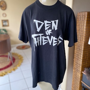 May include: Black t-shirt with a white graphic print of "Den of Thieves" in a stylized font.