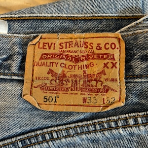 May include: A brown leather Levi Strauss & Co. patch with red text. The patch reads "Levi Strauss & Co. Original  Riveted Quality Clothing XX Trade Mark Patented in U.S. May 20 1947 Care Instructions Inside Garment 100% Cotton WPL 423 501 133 132".