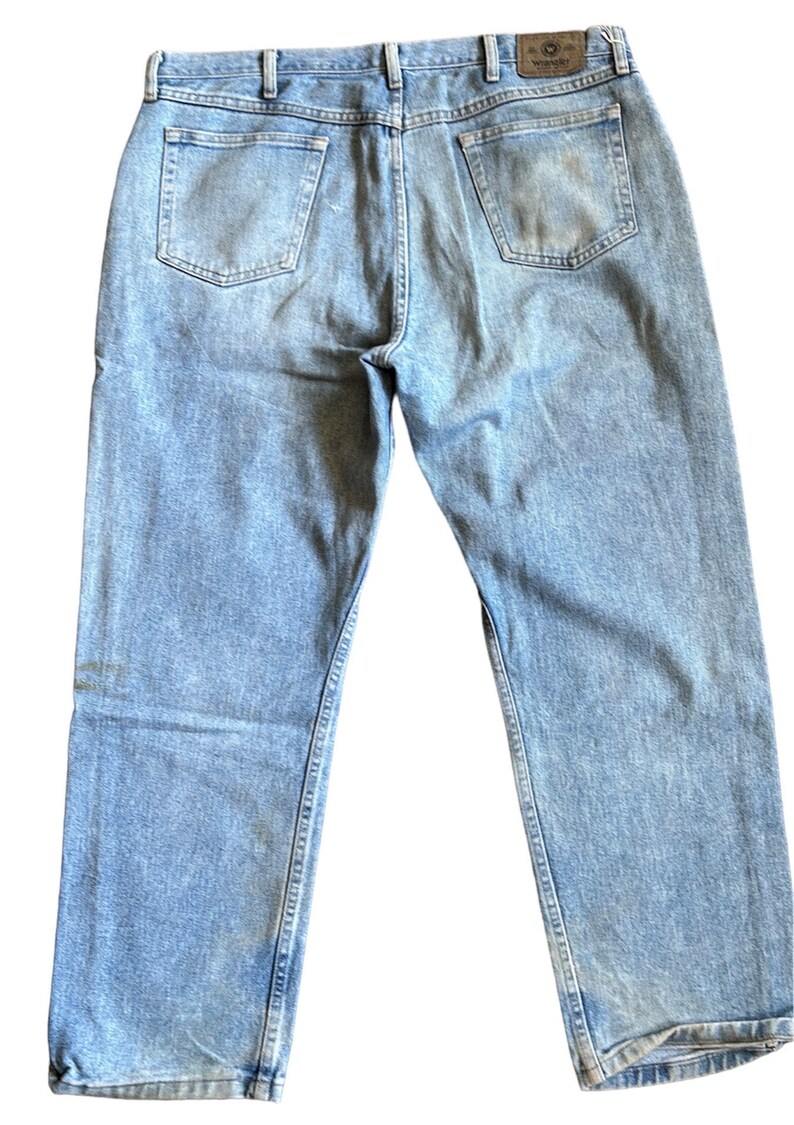 May include: Light blue denim jeans with a brown leather patch on the back waistband that says "Wrangler".