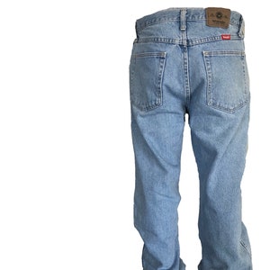 Puede incluir: Vaqueros de mezclilla azul claro con un dise&ntilde;o cl&aacute;sico de cinco bolsillos. Los vaqueros presentan un parche de cuero marr&oacute;n con el logotipo "Wrangler" en la cintura trasera. Los vaqueros tienen un corte relajado y est&aacute;n hechos de mezclilla duradera.