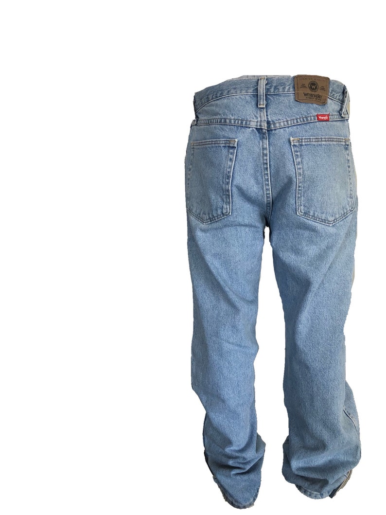 Puede incluir: Vaqueros de mezclilla azul claro con un dise&ntilde;o cl&aacute;sico de cinco bolsillos. Los vaqueros presentan un parche de cuero marr&oacute;n con el logotipo "Wrangler" en la cintura trasera. Los vaqueros tienen un corte relajado y est&aacute;n hechos de mezclilla duradera.