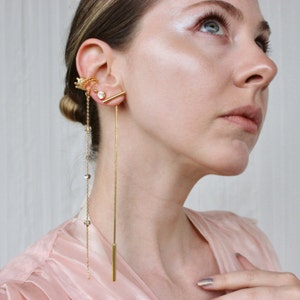 May include: Gold-toned ear jewelry set. The set includes a crown ear cuff, a stud earring with a clear stone, a linear earring, and a long chain earring with clear stones. The jewelry is worn on the ear.