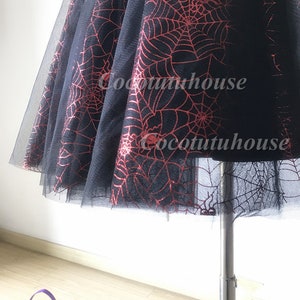 Pu&ograve; includere: Gonna di tulle nera con un motivo a ragnatela rosso. La gonna &egrave; su un manichino e ha una silhouette ampia e fluida.