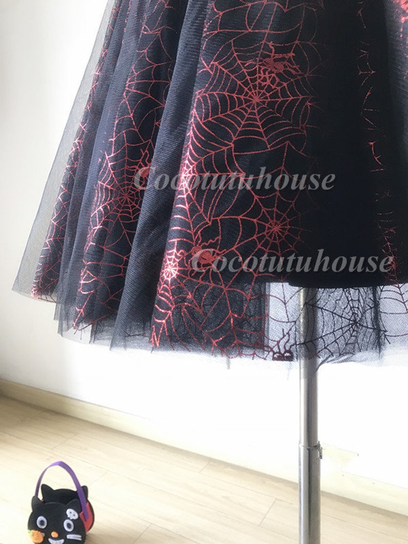 Pu&ograve; includere: Gonna di tulle nera con un motivo a ragnatela rosso. La gonna &egrave; su un manichino e ha una silhouette ampia e fluida.