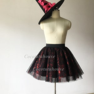 Pu&ograve; includere: Gonna di tulle nera con un motivo a ragnatela rosso. La gonna &egrave; su un manichino e ha una cintura nera. Un cappello da strega nero con un nastro rosa &egrave; sulla testa del manichino.