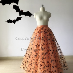 Pu&ograve; includere: Una lunga gonna di tulle arancione con una stampa di Halloween nera e arancione. La stampa presenta pipistrelli, zucche e cappelli da strega.