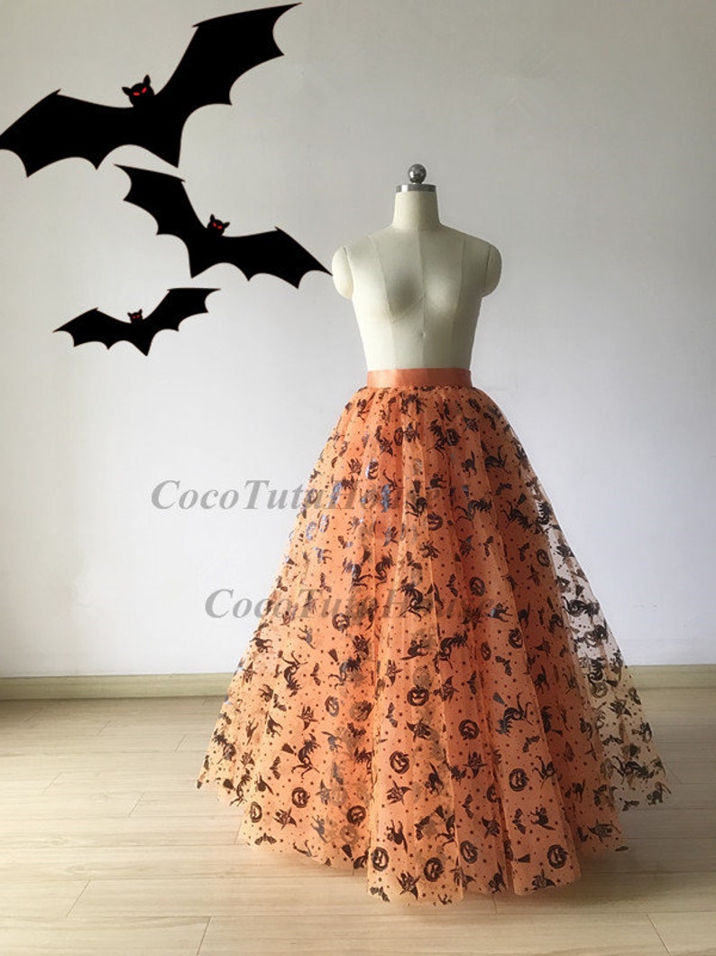 Pu&ograve; includere: Una lunga gonna di tulle arancione con una stampa di Halloween nera e arancione. La stampa presenta pipistrelli, zucche e cappelli da strega.
