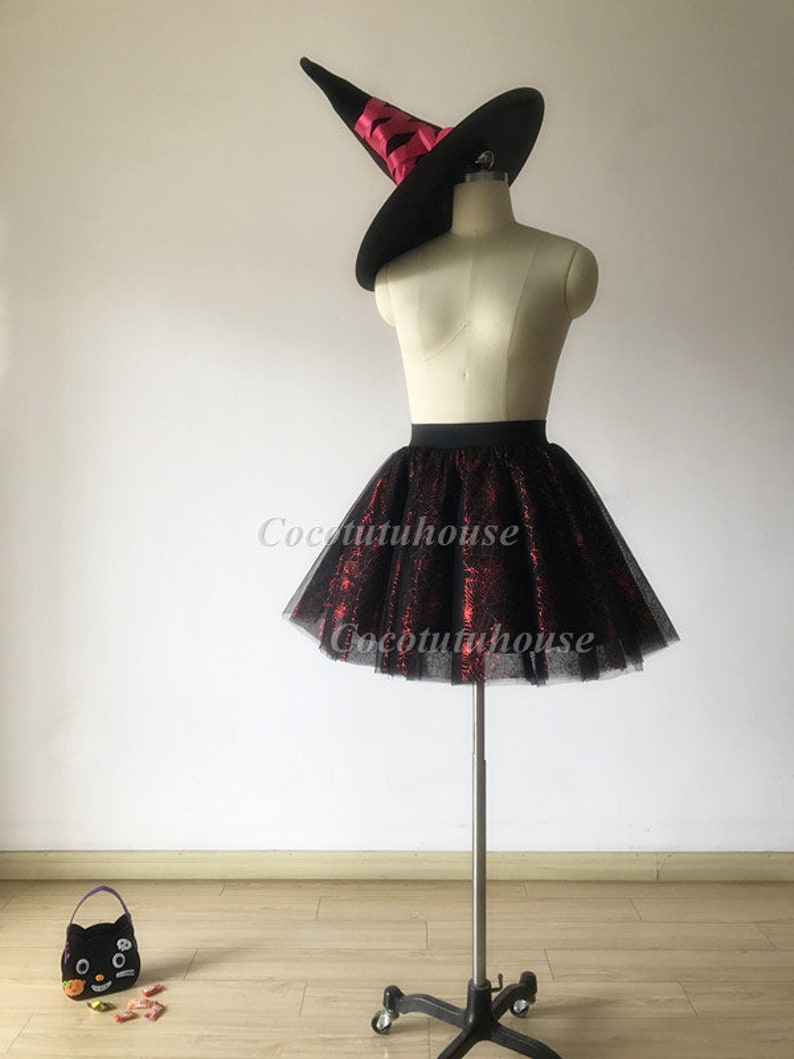 Pu&ograve; includere: Gonna di tulle nera con motivo a ragnatela rosso e un cappello da strega nero con un nastro rosso.